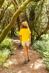 Selbstklebende Fototapeten Tourist woman walking in the natural park of La Llania in El Hierro, Canary Islands. On a path of laurel from El Hierro in a lush green landscape © unai