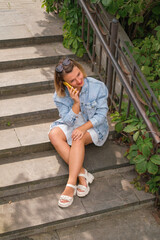 A woman in a blue denim jacket is talking on the phone sitting on the steps in the city courtyard