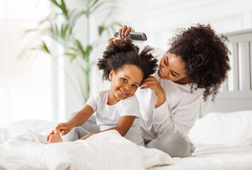 Happy ethnic family. African american mom brushing her little daughter's curly hair.