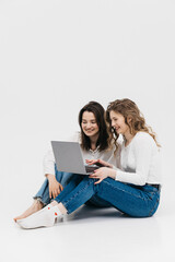Young happy couple of young women on white background communicate showing laptop together. Chroma...