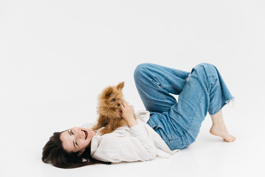 Happy woman lies on the floor with her dog. Charming dog sniffs something in front of him, lying on the lap of the girl. Young woman holding her curious puppy