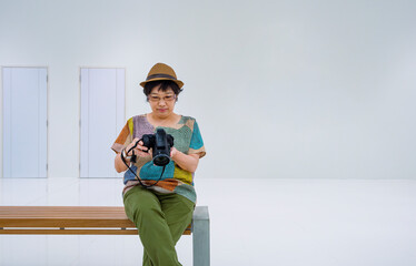 Asian female tourist checking photo on digital camera while sitting on wooden bench in white rest area of subway station