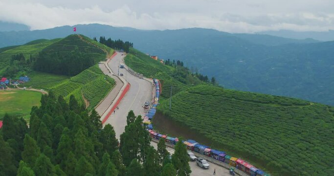 The drone takes a smooth flight over a popular tourist destination, the lush green tea gardens of Kanyam in Ilam, Nepal, showcasing a scenic highway winding through the verdant landscape.