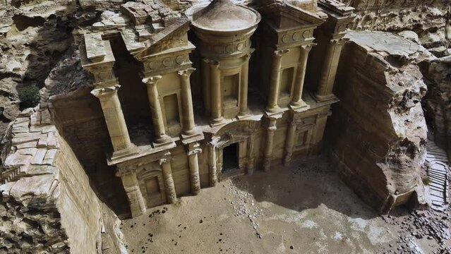 Aerial view away from the Ad Deir monastery, in sunny Petra, Jordan - reverse, tilt, drone shot