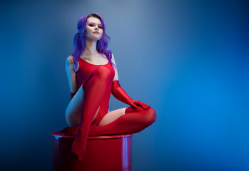 sexy girl in a red bodysuit, stockings and red gloves poses erotically on a blue background of a...
