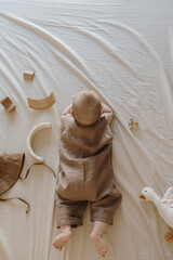 Fototapeta na wymiar Cute newborn baby in brown bodysuit lying on the bed with beige bed linens. Cute minimal baby fashion concept. Top view