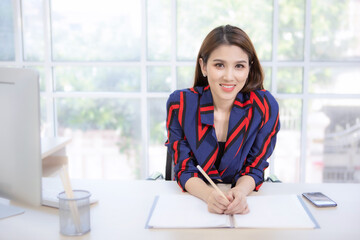 Young professional Asian businesswoman sitting thoughtfully with documents on the desk in her office.