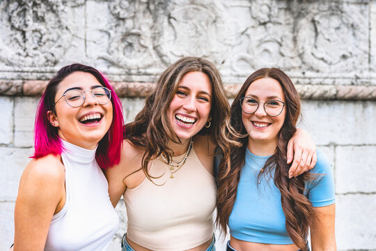 Happy three female friends laughing together-Young Multiracial women having fun and hugging each on city street outdoors -Millennial Girls Friendship Lifestyle Concept-Youth Culture with trendy people