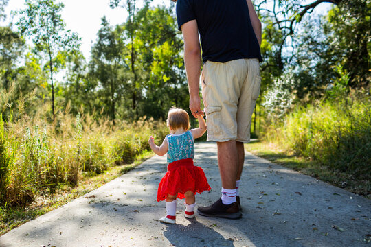 Toddler holding fathers hand walking down path in morning getting family exercise