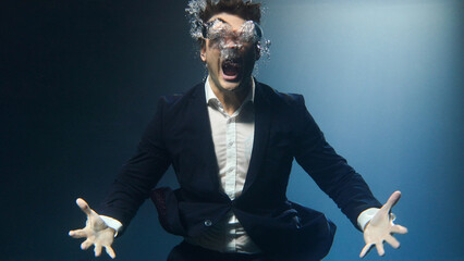 A businessman, a man in a suit, screams underwater.