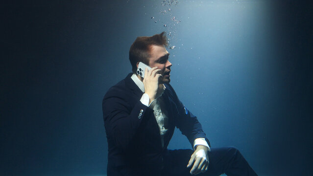 Businessman, a man in a suit, is talking on a mobile phone underwater. - Powered by Adobe