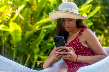 Woman in a hat sitting and relaxing in an outdoor park enjoying her cell phone while using social media. This is Valladolid park in Yucatan, Mexico.