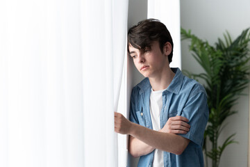 Sad teenager boy looking through window