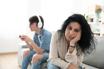 Despaired mother sitting on sofa while son is gaming