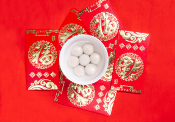 Tangyuan and red envelopes are on the table with red background, festive image, Lantern...