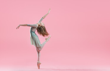 elegant young ballerina in pointe shoes dancing on a delicate pink background