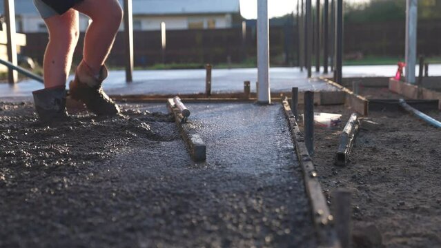 Contractor smoothing fresh concrete surface of residential driveway with wooden float