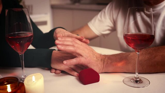 Close-up of couples hands giving support and love. Senior couple having romantic dinner at home in kitchen with wine and presents. Concept of love, relationship, family, emotions, support and care