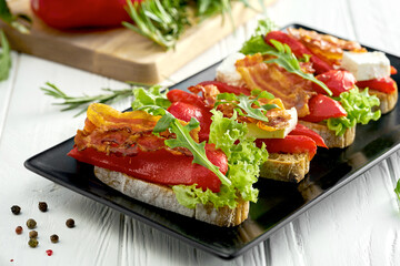 Bruschetta with bell pepper and bacon, feta cheese in a black plate on a white background