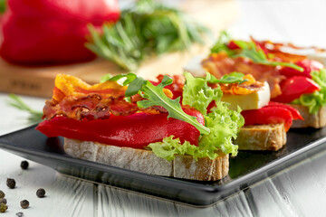 Bruschetta with bell pepper and bacon, feta cheese in a black plate on a white background