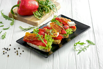Bruschetta with bell pepper and bacon, feta cheese in a black plate on a white background