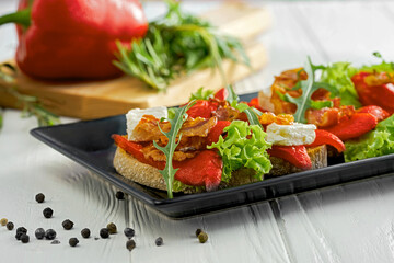 Bruschetta with bell pepper and bacon, feta cheese in a black plate on a white background
