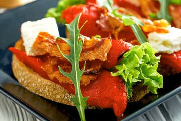 Bruschetta with bell pepper and bacon, feta cheese in a black plate on a white background