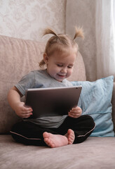 Happy little child sitting on sofa and using tablet.