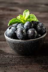 Top view of bowl with blueberries with water drops with mint leaves, on table, dark background, vertical, with copy space
