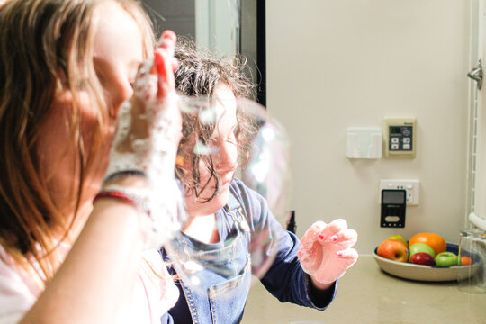 Two girls blowing bubbles in the kitchen