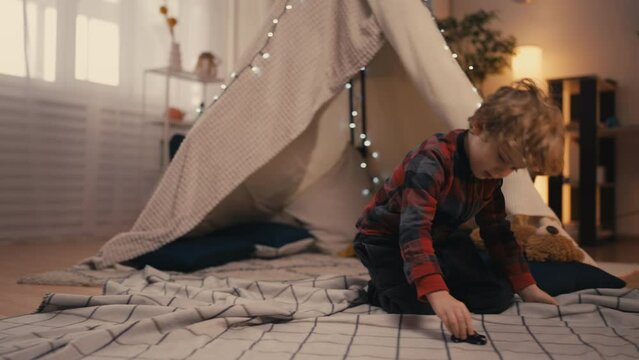 Cute little boy playing with a toy car in a blanket fort at home, imagination