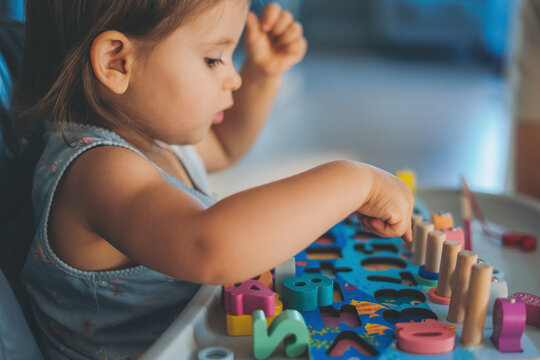 Side view of a baby girl learning numbers through gam, activity with wooden numbers. Toy to learn counting and stimulate imagination, creativity. Education