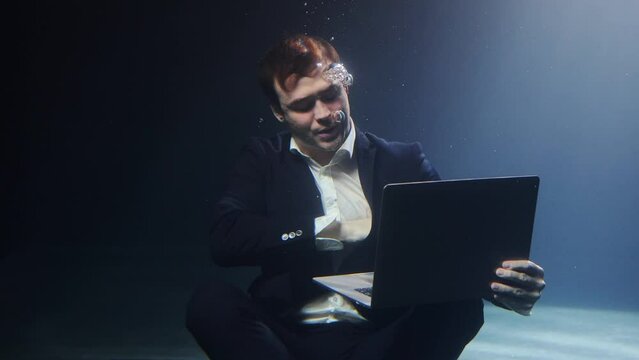 A businessman in a suit is working on a laptop underwater.