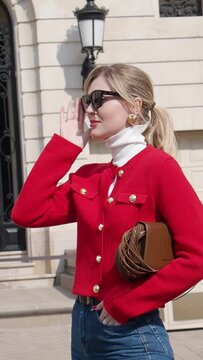 Outdoor portrait of young elegant fashionable woman puts on sunglasses, wears colorful red blazer, leather bag, turtleneck stands in European city street. Clothes Trends of spring and summer