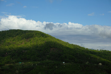 General plan of green hills illuminated by sun rays breaking through the clouds against the blue sky in the summer season