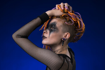 Young woman with orange color braids hairdo and horror black stage make up painted on face. Studio shot on blue background. Part of photo series