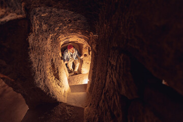 Tourist man in Kaymakli underground city ancient cave in Cappadocia, Turkey - obrazy, fototapety, plakaty