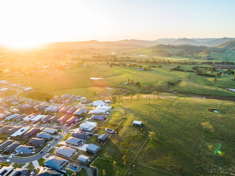 Aerial view at sunset over houses at the edge of town with paddock farmland backyard