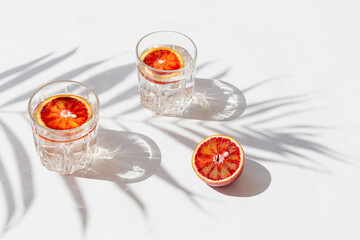 Creative composition made of half bloody red orange and two glasses with cocktail on white...