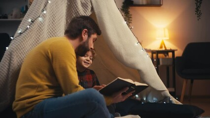 Dad encouraging little son to read, family spending time in a blanket fort