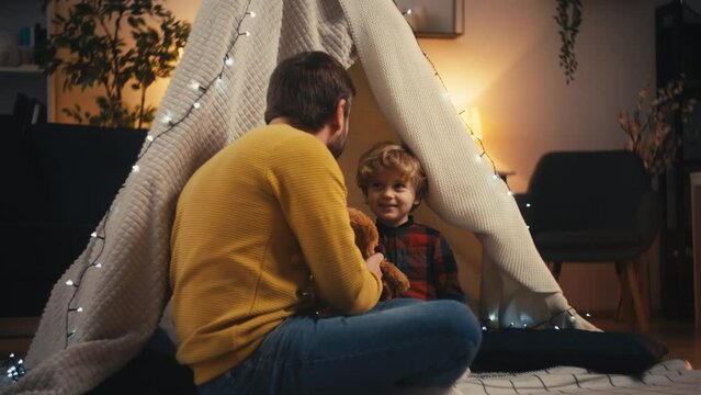 Father and little son playing with teddy bear in a blanket fort, togetherness