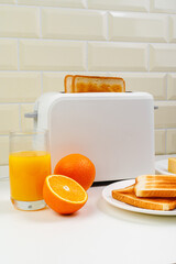 Healthy breakfast in the kitchen. Toaster and bread toast, freshly squeezed orange juice. Cheese, butter, lettuce. White toaster with healthy food and drinks on table in light kitchen
