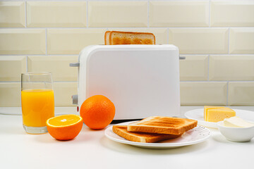 Healthy breakfast in the kitchen. Toaster and bread toast, freshly squeezed orange juice. Cheese, butter, lettuce. White toaster with healthy food and drinks on table in light kitchen