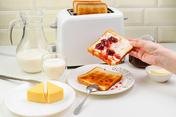 Useful breakfast. A young woman spreads jam on toast. Toaster and bread toast, milk, jam, cheese, butter. top view