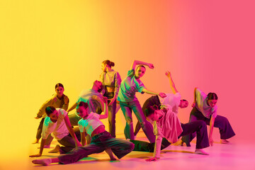 Group of young charming girls, dancers moving to the beat of the music on pink and yellow gradient background in neon light. Experimental dance