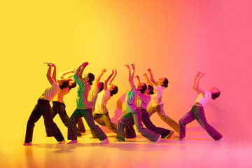 Group of beautiful teenage girls wearing white t-shirt, jeans dancing together on pink and yellow gradient background in neon light. Process of dance training