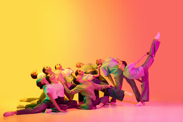 Group of pretty teenage girls wearing white t-shirt and jeans dancing together on pink and yellow gradient background in neon light. Children's choreography