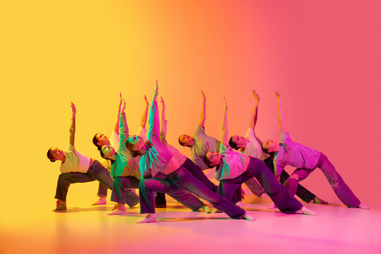 Group of beautiful teenage girls wearing white t-shirt and jeans dancing together on pink and yellow gradient background in neon light. Synchronicity