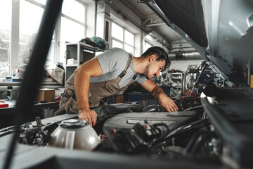 Young male mechanic examining engine under hood of car at the repair garage