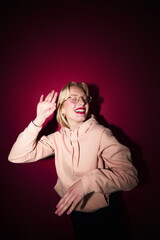 A cheerful young blond woman dancing in studio isolated on magenta background. Viva magenta, color of the year.